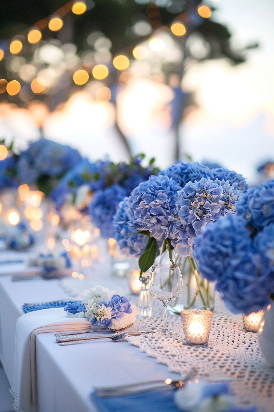 Blue themed glamping. Indigo hydrangea centerpieces on white, crochet table cloth under seaside sunset lighting.