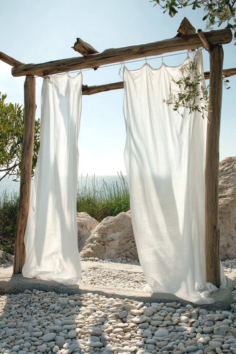 Outdoor shower setup. Driftwood frame with white sheer curtains and pebble floor.